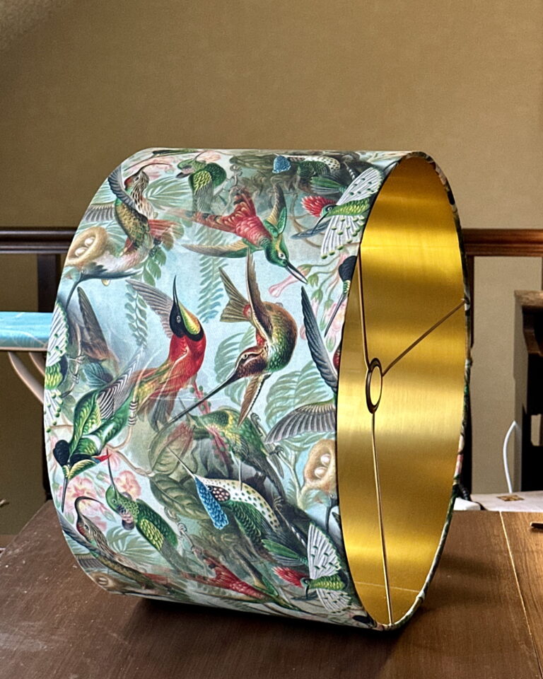Tropical hummingbird pattern glowing through brushed gold interior lampshade