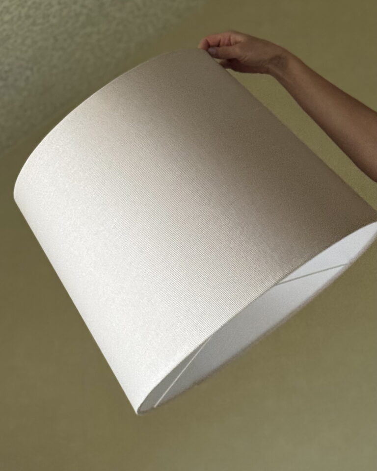 Minimalist beige textured fabric lampshade held in hand, neutral background