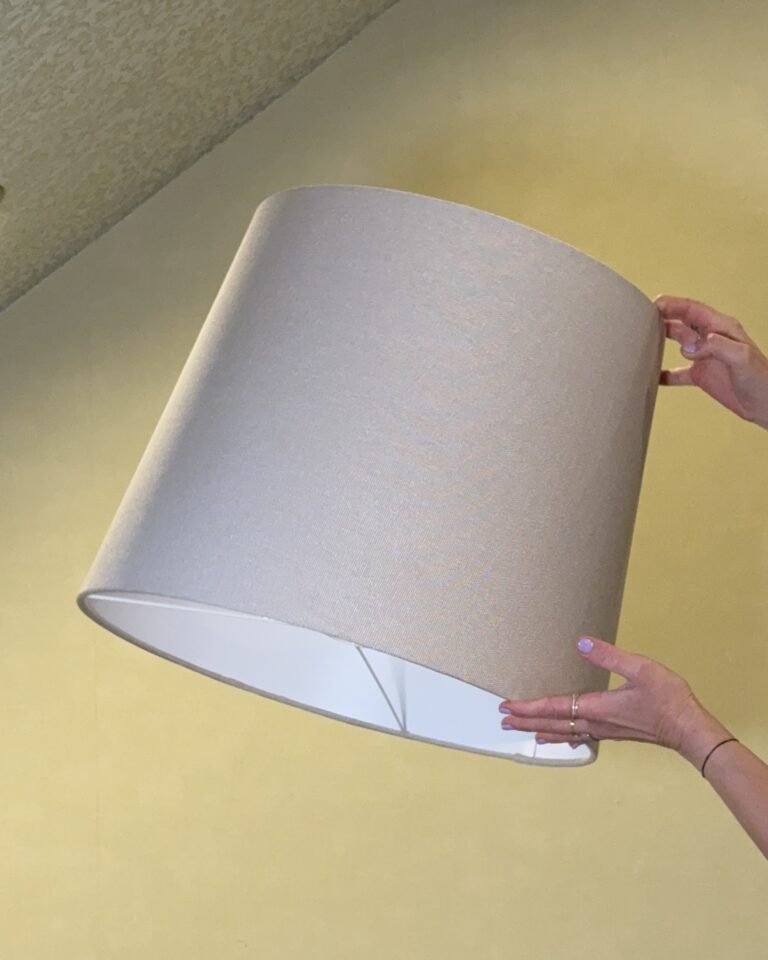Large textured beige lampshade held from below showing subtle fabric texture and frame detail