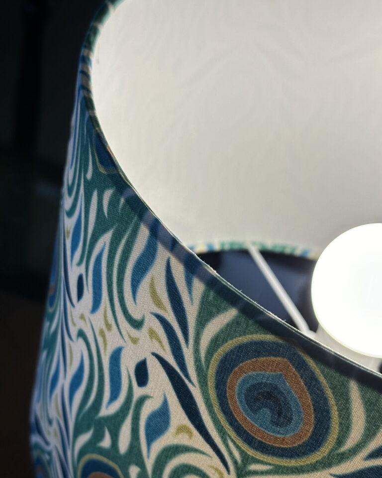 Art Deco Peacock Table Lamp glowing softly with peacock-feather pattern fabric, handcrafted by Chantier Studio.